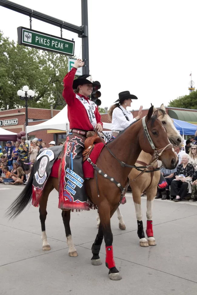 horseback rider in parade and pikes peak road sign in background