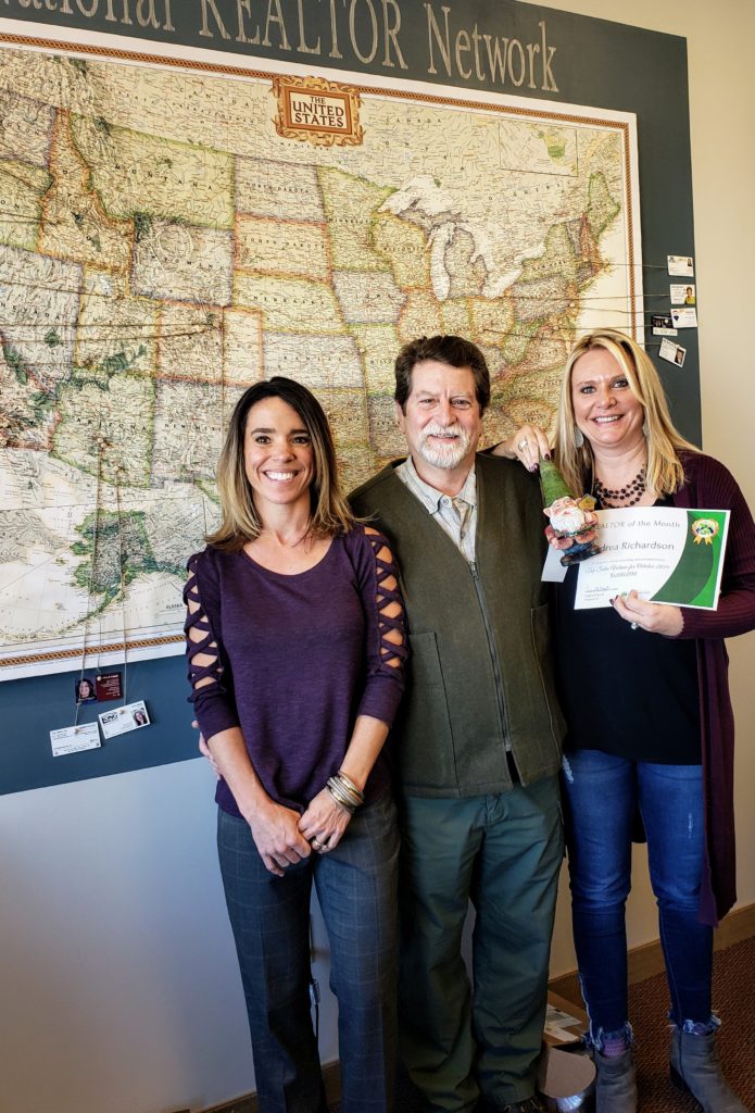 realtors andrea richardson, dr bob osgood and joy mcwilliams standing in front of map of united states. Andrea holding award for top sales