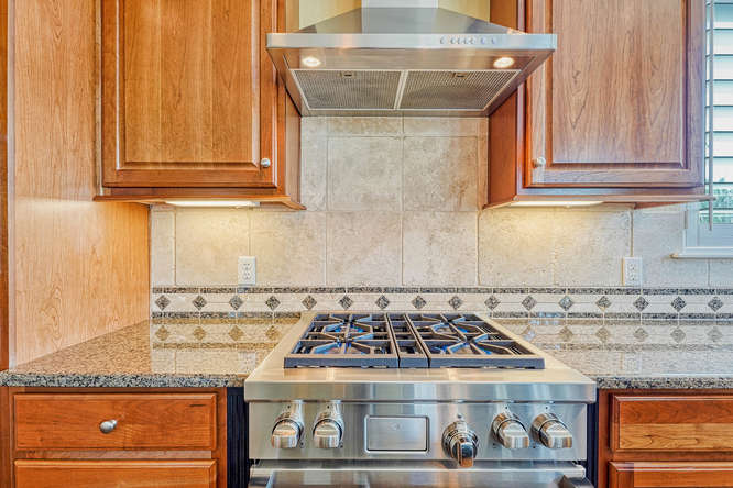 4 burner gas cooktop with stainless steel hood and custom stone backspash